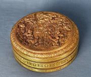 Caja circular de bronce cincelado, con personajes y paisaje en relieve.