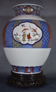 Vaso porcelana oriental, blano con guardas. Reservas con personajes. Base de madera. Alto: 33 cm.