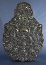 Placa de plata colonial, con decoración cincelada de, putino, aves y volutas. Montada sobre una madera. Alto: 38 cm.