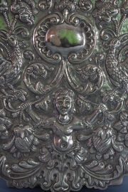 Placa de plata colonial, con decoración cincelada de, putino, aves y volutas. Montada sobre una madera. Alto: 38 cm.